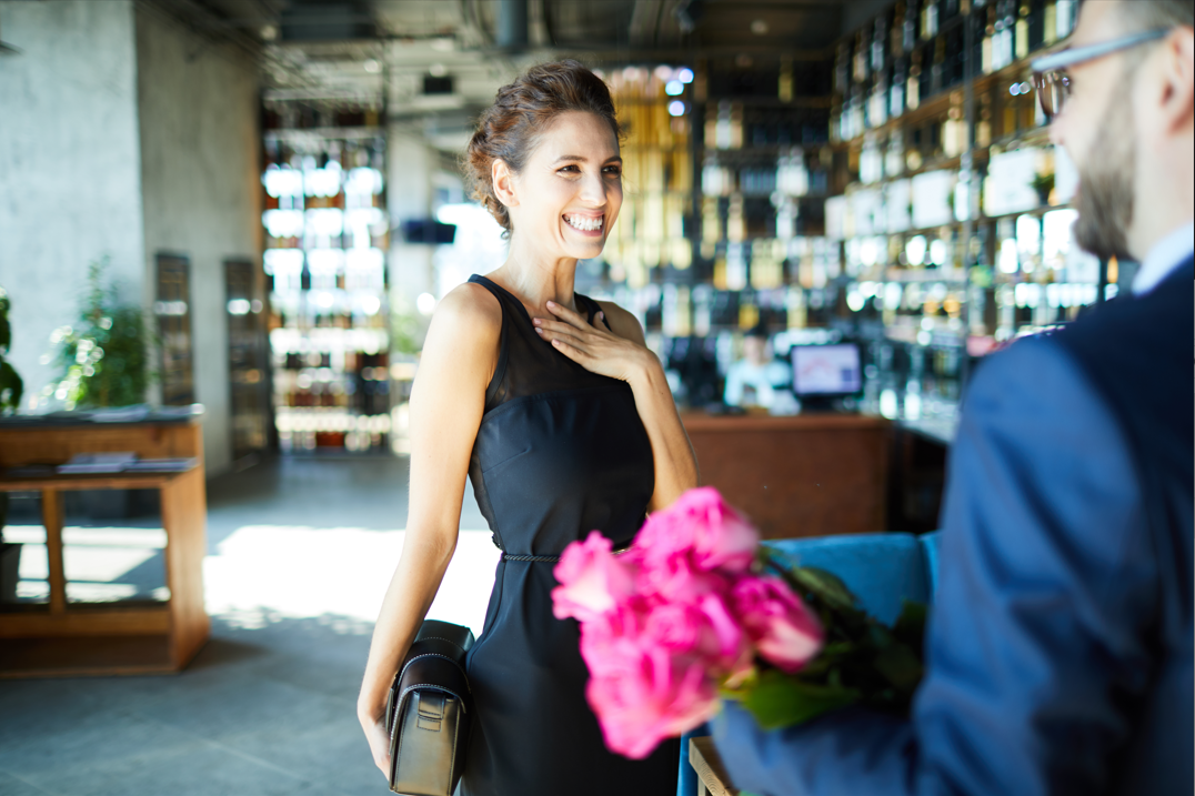 Alkalmi ruhába öltözött boldog hölgy virágot kap egy elegáns megjelenésű úrtól.